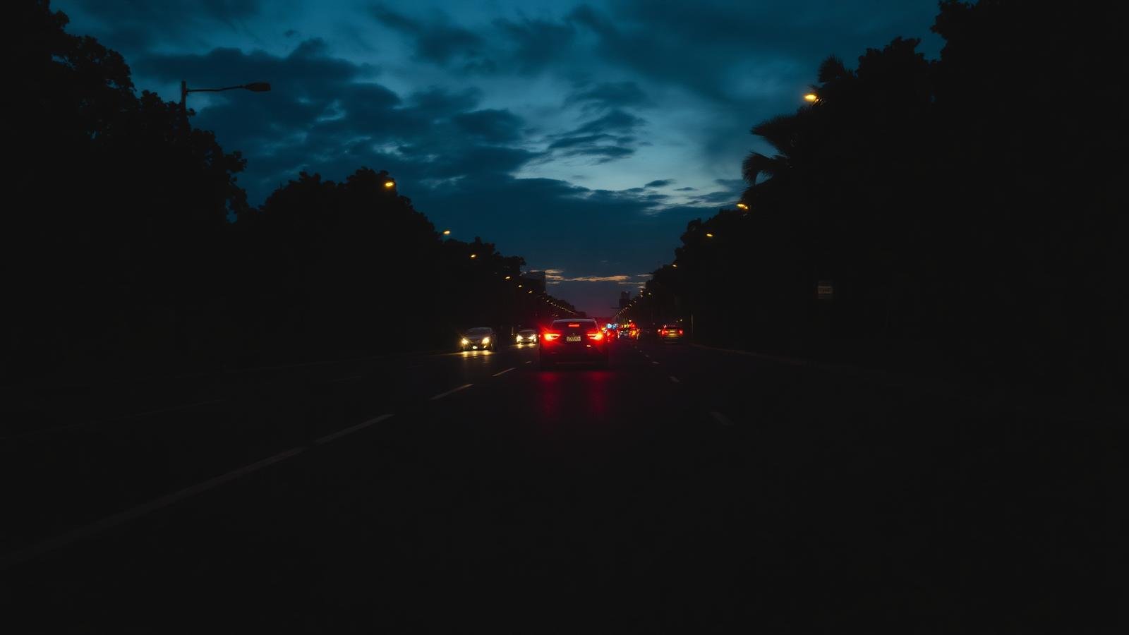Avenida urbana ao anoitecer com veículo parado no acostamento.